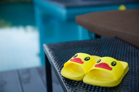 Yellow sandals duckling for kid on table beside the beach and swimming poolの写真素材