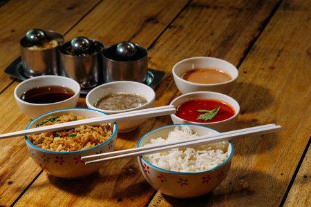 Bowls of rice with sauce and chopsticks on wooden tableの写真素材