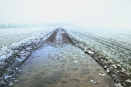 Winter frozen field road with cracked ice. Misty winter landscape with snowy field and frozen roadの写真素材