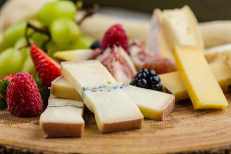Cheese plate with bread grapes and strawberries in a wooden desk on marble surface.