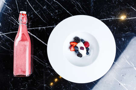 Vanilla ice cream scoops with fresh berries served in the white plate with the black background and bottle with strawberry jamの写真素材