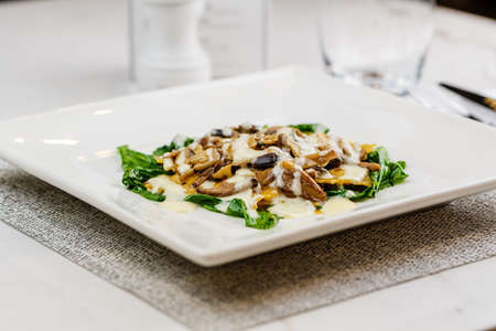 Italian ravioli with fresh roasted mushrooms and creamy parmesan cheese sauce decorated with spinach on white plate.の写真素材