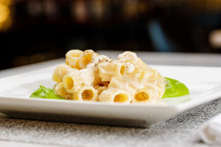 Penne pasta with a creamy sauce with parmesan cheese and spinach sause on a white plate on a marble surfaceの写真素材