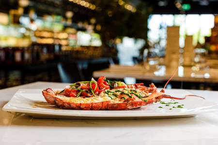 Italian cuisine. Whole lobster baked and sliced in half Served with tomato salad and sauce on white plateの写真素材