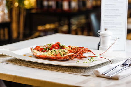 Italian cuisine. Whole lobster baked and sliced in half Served with tomato salad and sauce on white plateの写真素材
