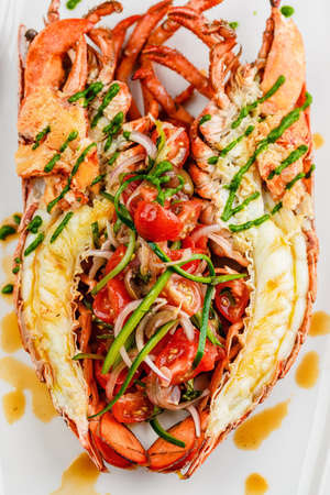 Italian cuisine. Whole lobster baked and sliced in half Served with tomato salad and sauce on white plateの写真素材