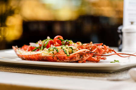 Italian cuisine. Whole lobster baked and sliced in half Served with tomato salad and sauce on white plateの写真素材