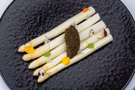 White asparagus served with caviar decorated with flowers on black plate.の写真素材