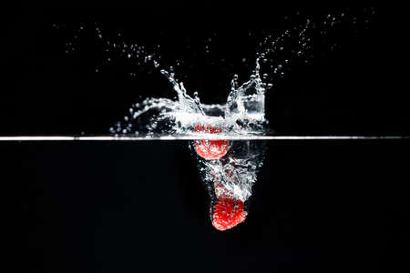 Two raspberrys falls deeply under water with a big splash.の写真素材