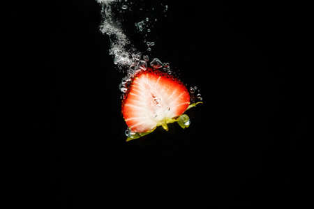 Half a strawberry splashing into waterの写真素材