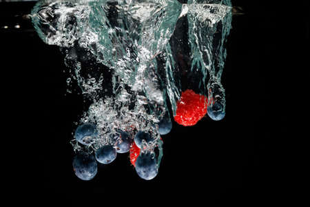 Raspberrys and blueberry falls deeply under water with a big splash.の写真素材