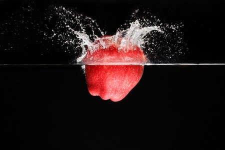 A apple falls deeply under water with a big splash.の写真素材