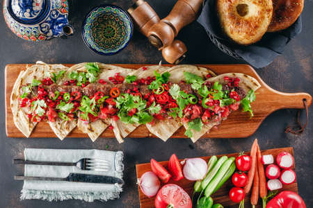 Lula Kebab on the wooden service plank with garnet, coriander and Arabic bread surrounded with vegetablesの写真素材