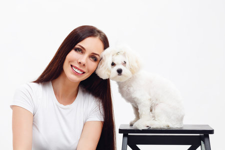 Beautiful brunette girl with long hair sits next to white Maltese puppy and smiling with the teeth