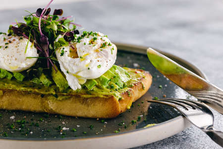 Guacamole and poached egg bruschetta served with greens and sliced avocadoの写真素材