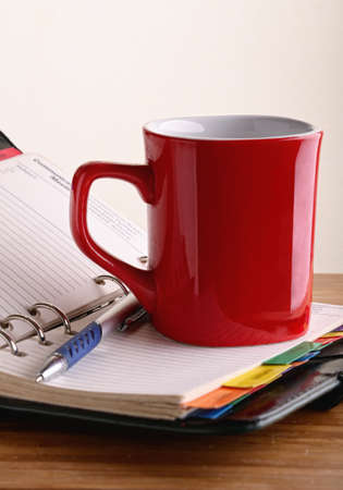 red mug of coffee in the open notepad next to the penの写真素材