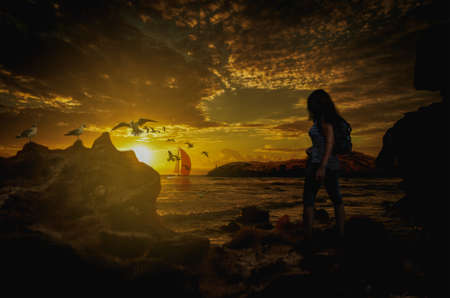 Silhouette of a lonely girl on the bank looking at the sunset over the waterの写真素材