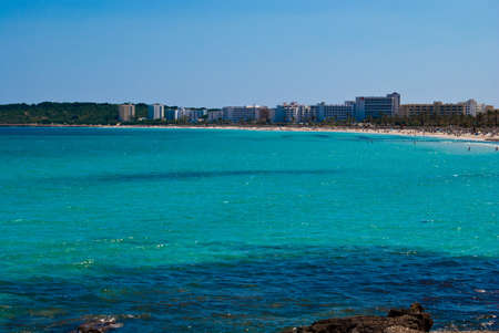 Mediterranean Sea bay under solid blue sky and Cala Millor resort town on Majorca island in Spainの写真素材