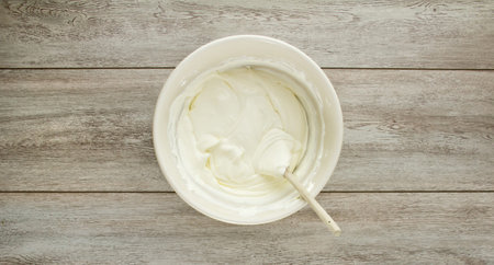 A ceramic ivory mixing bowl of cream soft cheese, mixed with a wood spoon on weathered boards.の写真素材