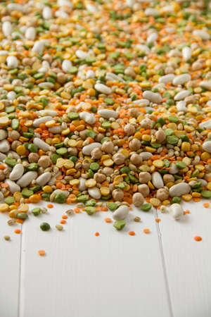 Mixed grains, pulses, beans, peas and legumes, spilling onto white painted woodの写真素材