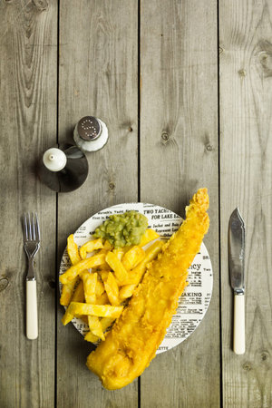 Traditional British takeaway meal of fish and chips with mushy peas on a newsprint plate