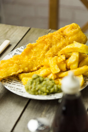 Traditional British takeaway meal of fish and chips with mushy peas on a newsprint plate