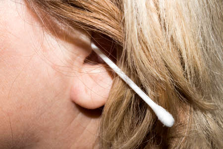 A woman cleans her ears with a cotton swab. Background man cleans ears.の写真素材
