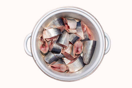 Salted herring in a saucepan, cut into chunks on a white background. Background of pieces of pickled herring top view.の写真素材