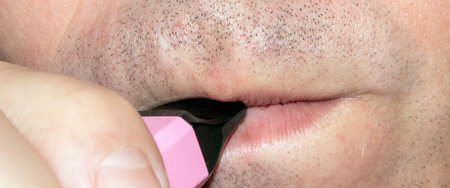 A man smokes an electronic cigarette. The electronic cigarette is disposable. Vape smoking. Vape with strawberries and ice cream.の写真素材