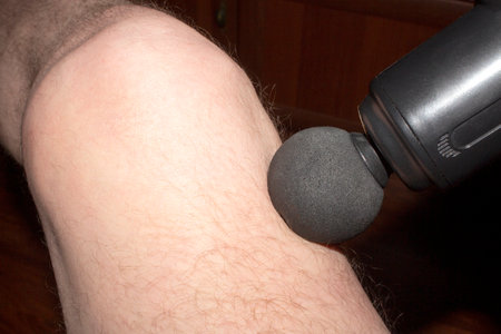 Knee joint massage with a vibrating massager. Home massage. Massage background.の写真素材