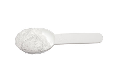 Creatine in a measuring plastic spoon on a white background.Creatine monohydrate.Creatine for endurance in training.Creatine powder background.の写真素材