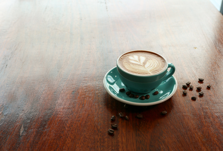 Hot coffee with leaf shape latte art and coffee bean on the wooden tableの写真素材