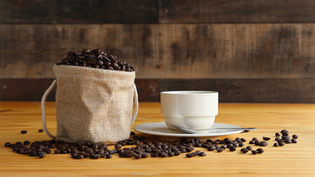 A cup of hot coffee with roasted coffee beans in warm light with wood backgroundの写真素材