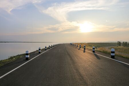 Road at Phra Satung water reservoir against sky during sunsetの写真素材