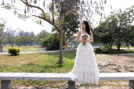 Asian bride in white bridal gown holding a lovely bouquet in a gardenの写真素材