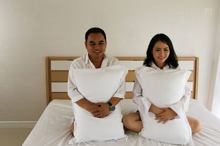 Happy Asian couple hold pillow on the bedの写真素材