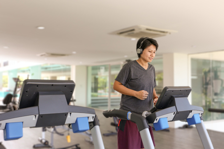 Happy Asian woman with bluetooth headphone work out in gym on treadmillの写真素材