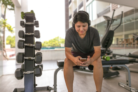 Happy Asian woman work out in gym use mobile phone and bluetooth headphoneの写真素材