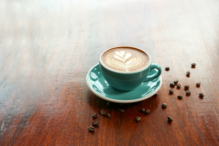Hot coffee with leaf shape latte art and coffee bean on the wooden tableの写真素材