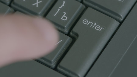 CloseUp View of a Hand Actively Pressing the Enter Key on a Computer Keyboard Deviceの写真素材