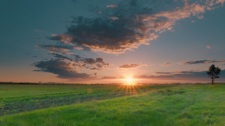 Breathtakingly stunning sunset over lush green fields, accompanied by majestic clouds above Time lapse.の写真素材