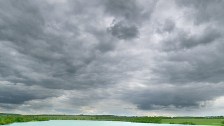 A Dramatic and Overcast Cloudy Sky Spreads Across a Calm and Tranquil Water Landscape During Dusk Time lapse.の写真素材