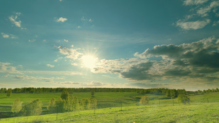 A beautiful serene landscape featuring sunlit green fields, fluffy clouds and natures grace Time lapse.の写真素材