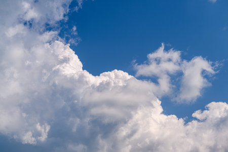 Fluffy white clouds drift gracefully across a bright and vibrant blue sky above us
