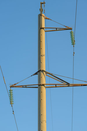 A utility power pole is prominently silhouetted against a bright blue sky with clouds