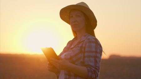 A woman is using a tablet while standing in a serene field during a beautiful sunset