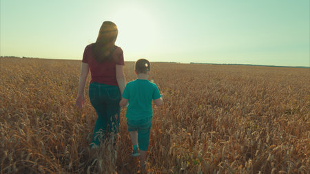 Strolling through a golden field with a joyful child, enjoying nature and making memoriesの写真素材