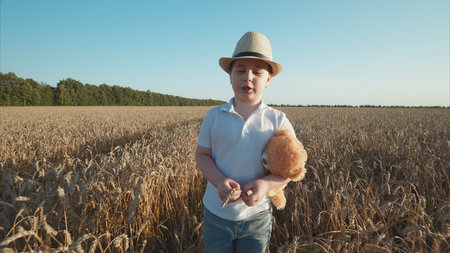 A child in a wheat field joyfully holding a teddy bear, embodying innocence and adventureの写真素材