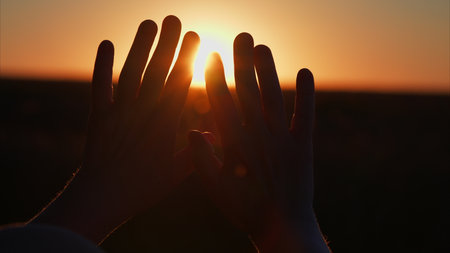 Silhouetted Hands Reaching for the Magical Sunset Over the Tranquil Horizon in the Eveningの写真素材