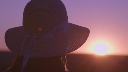 The beautiful silhouette of a person peacefully watching the stunning sunset while wearing a hatの写真素材